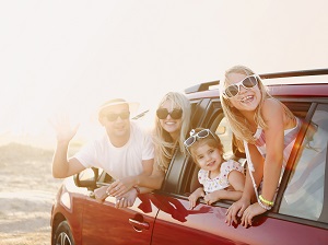 family of 4 smiling at camera on vacation, sitting in a car